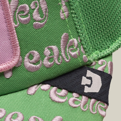 Close-up of the Freaky Friday cap by Goorin Bros.—green fabric with pink embroidered text and a black tag sporting a white geometric logo. A fresh Friday drop made for bold weirdos eager to flaunt their wild side.