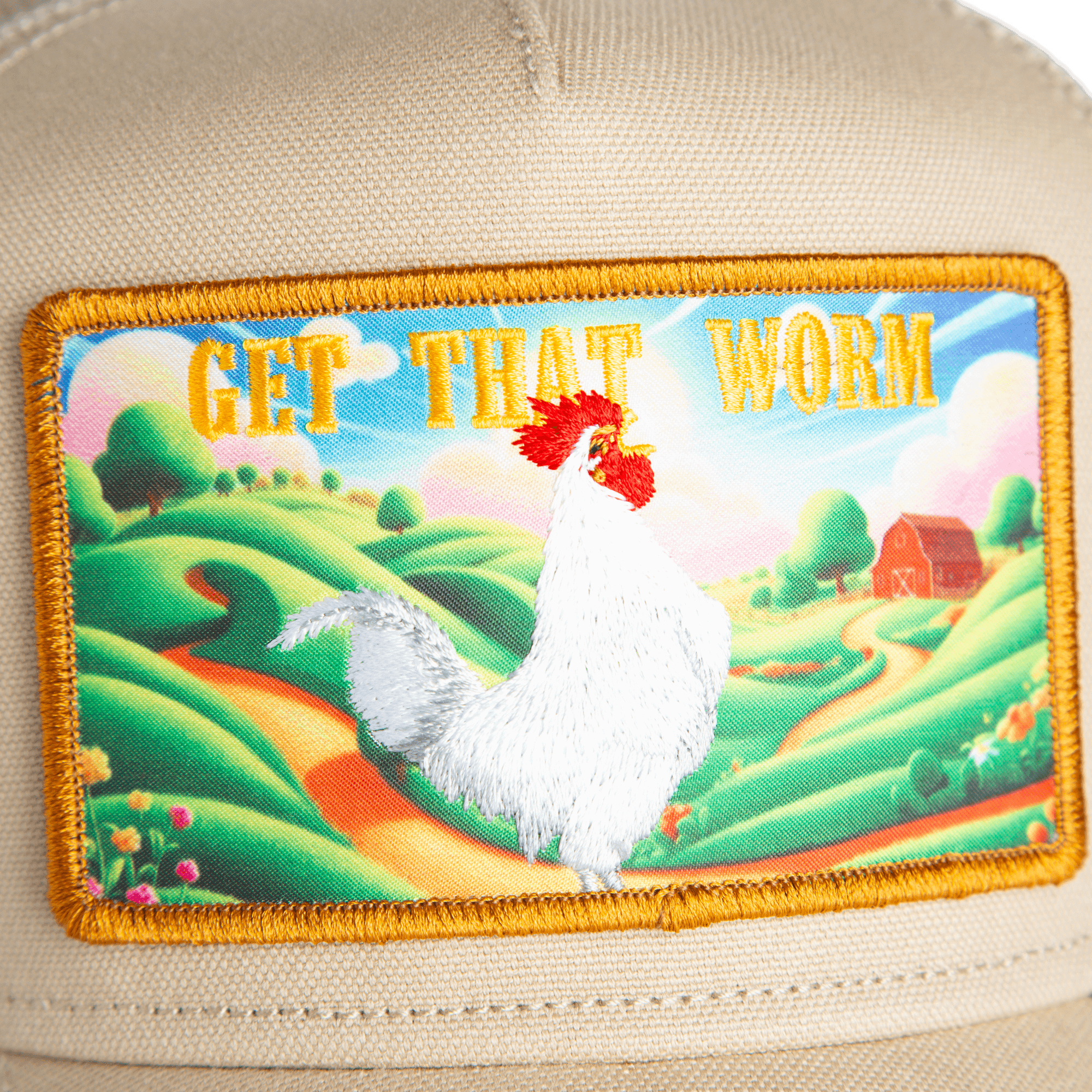 A close-up of the Greener Grass - Get that Worm trucker hat by Goorin Bros., showing a fabric patch with a white chicken, scenic farm landscape, and "GET THAT WORM" in bold yellow on beige.