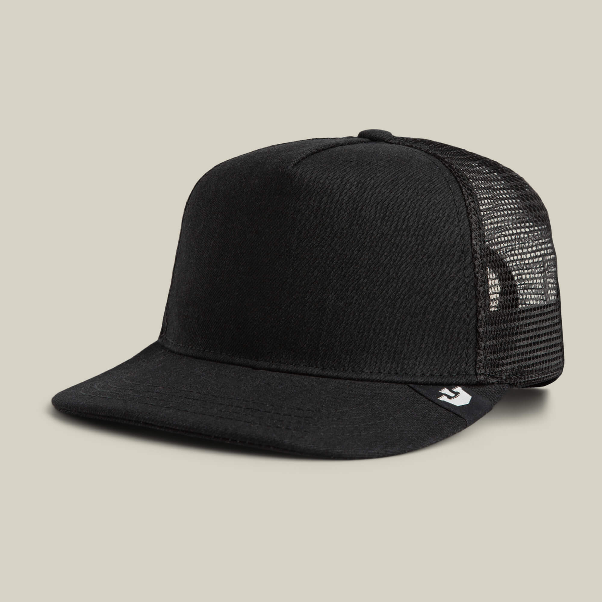 The Clean Denim Trucker by Goorin Bros. features a black denim front, solid flat brim, and black mesh back, displayed on a plain beige background. Made in the USA for a clean, classic look.