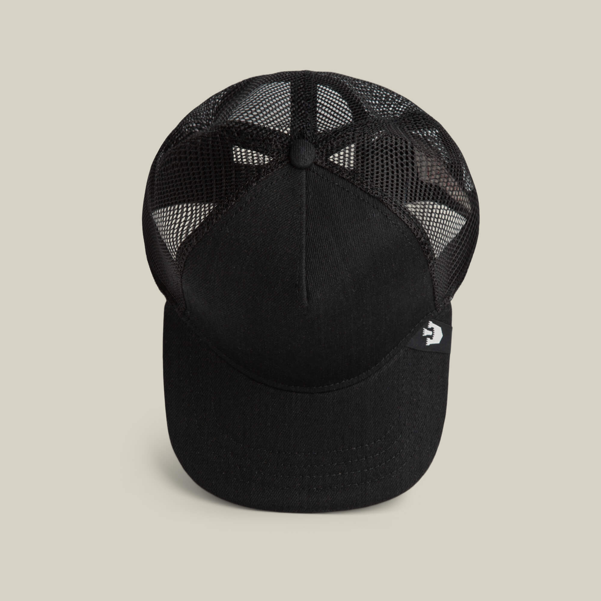 The Clean Denim Trucker by Goorin Bros. is a black mesh trucker hat with a solid front panel and curved brim, made in the USA. A small side tag with a white logo adds a classic touch. Shown from above on a neutral background.