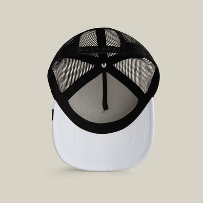 The Clean Denim Trucker by Goorin Bros. features a black mesh back, white front panel and brim, shown from below on a beige background. This hat updates classic style with a modern touch.