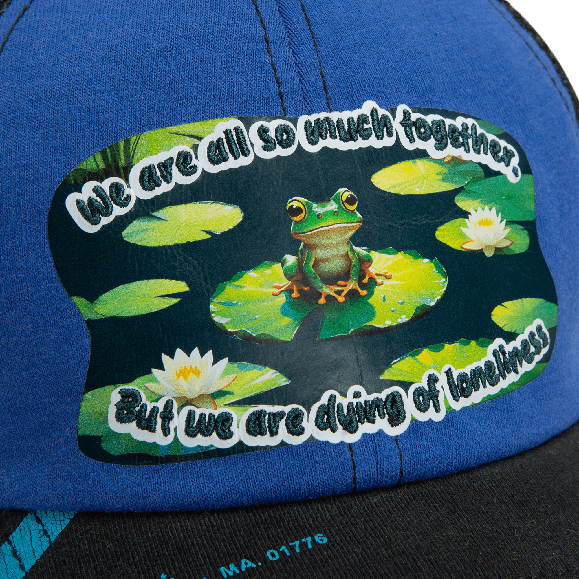A sticker on the blue Lil Sohei cap by Goorin Bros. shows a frog on a lily pad among water lilies with the text: We are all so much together. But we are dying of loneliness. Explore unique hats that tell your story.