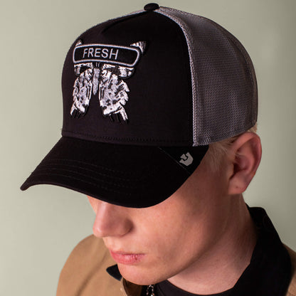In a close-up portrait, a person wearing the Goorin Bros. Classic Rocker - Fresh cap—a black and grey mesh hat with FRESH and two embroidered eagle heads—shows confident night mode vibes while looking downward.