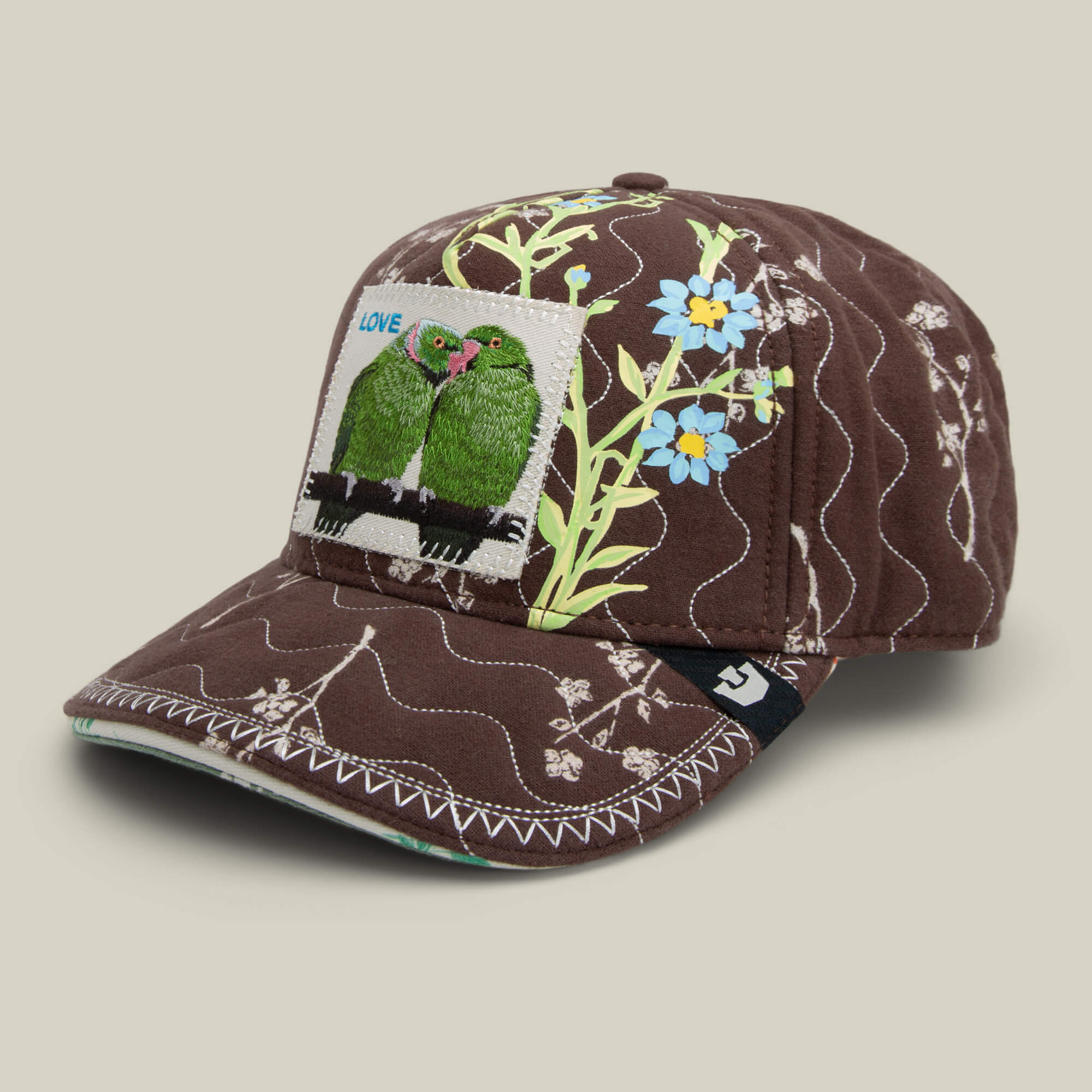 The Goorin Bros. Vol. 1 - Quiltbag: Love is a chocolate brown OG Trucker cap with quilted fabric, floral embroidery, and a front patch with two green birds and LOVE label.