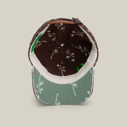 A top-down view of the Goorin Bros. Vol. 1 - Quiltbag: Love cap shows a chocolate brown quilted interior with white floral prints and a green brim featuring hand-stitched flower designs.