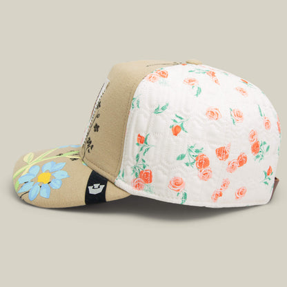 The Goorin Bros. Vol. 1 - Quiltbag: Live is a tan and white OG Trucker hat with a quilted floral pattern, pink rose accents, a bold blue daisy on the brim, and detailed floral embroidery for extra charm.