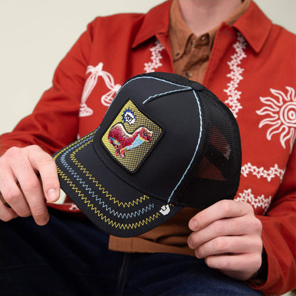 A person in an orange embroidered jacket holds Goorin Bros.' "All Around the Mulberry Bush"—a Pop Art trucker hat with a black mesh back and a colorful dodo bird patch on the front, exuding bold style and playful charm.