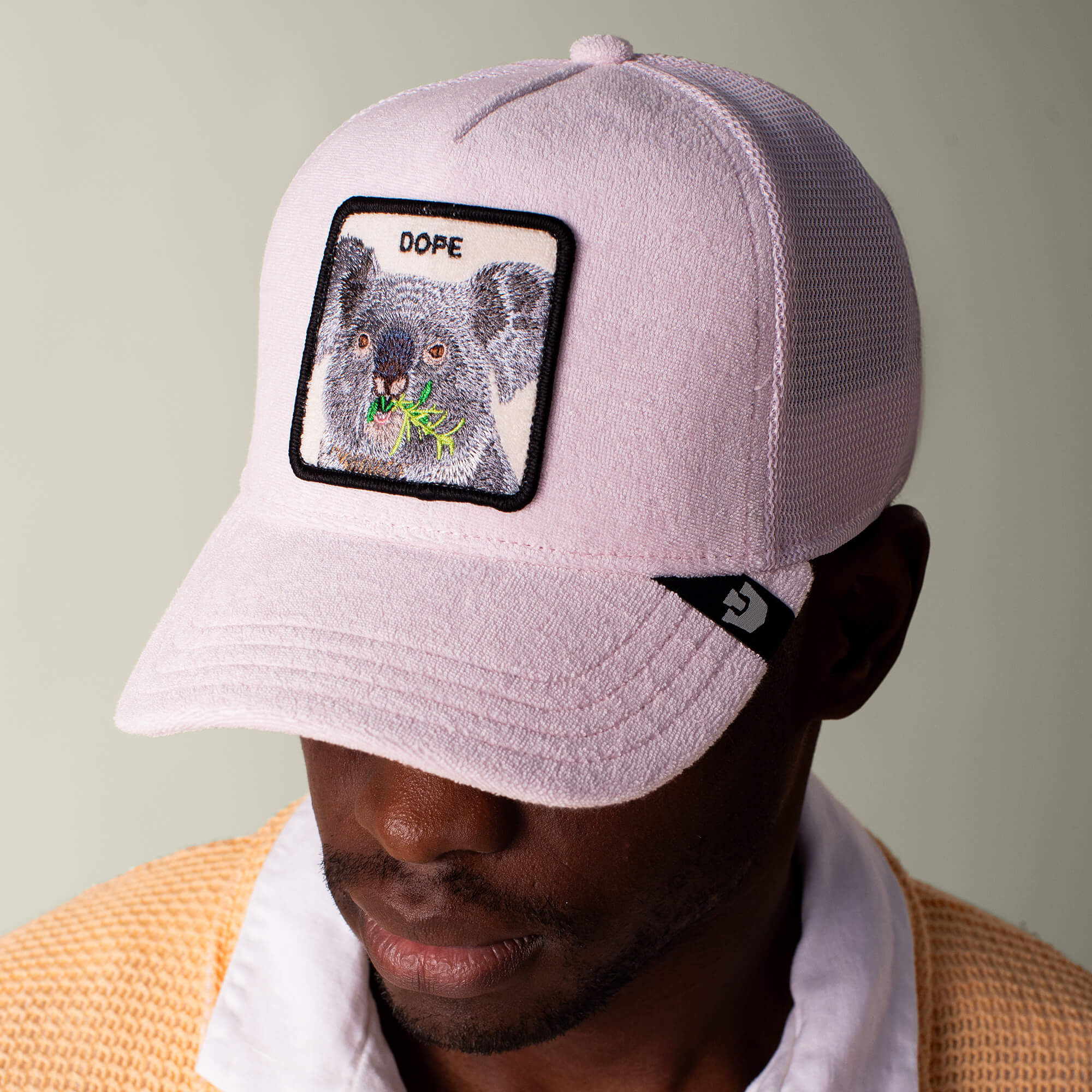 A person wearing the Goorin Bros. Terry Cloth Koala hat in pale pink, featuring a koala design with "DOPE" embroidered above it, looks downward.