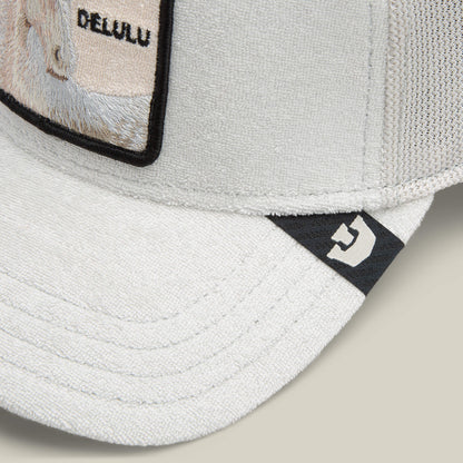 Close-up of the Goorin Bros. Terry Cloth Unicorn cap in light gray, made from soft fabric, with a rectangular patch reading DELULU and a small black logo tag on the brim.