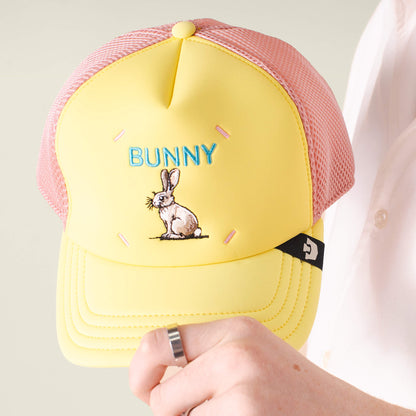A hand holds the Goorin Bros. Neo Farm - Bunny Rabbit hat, featuring a playful yellow and pink mesh design, an embroidered bunny and "BUNNY" in blue—perfect for everyday wear.