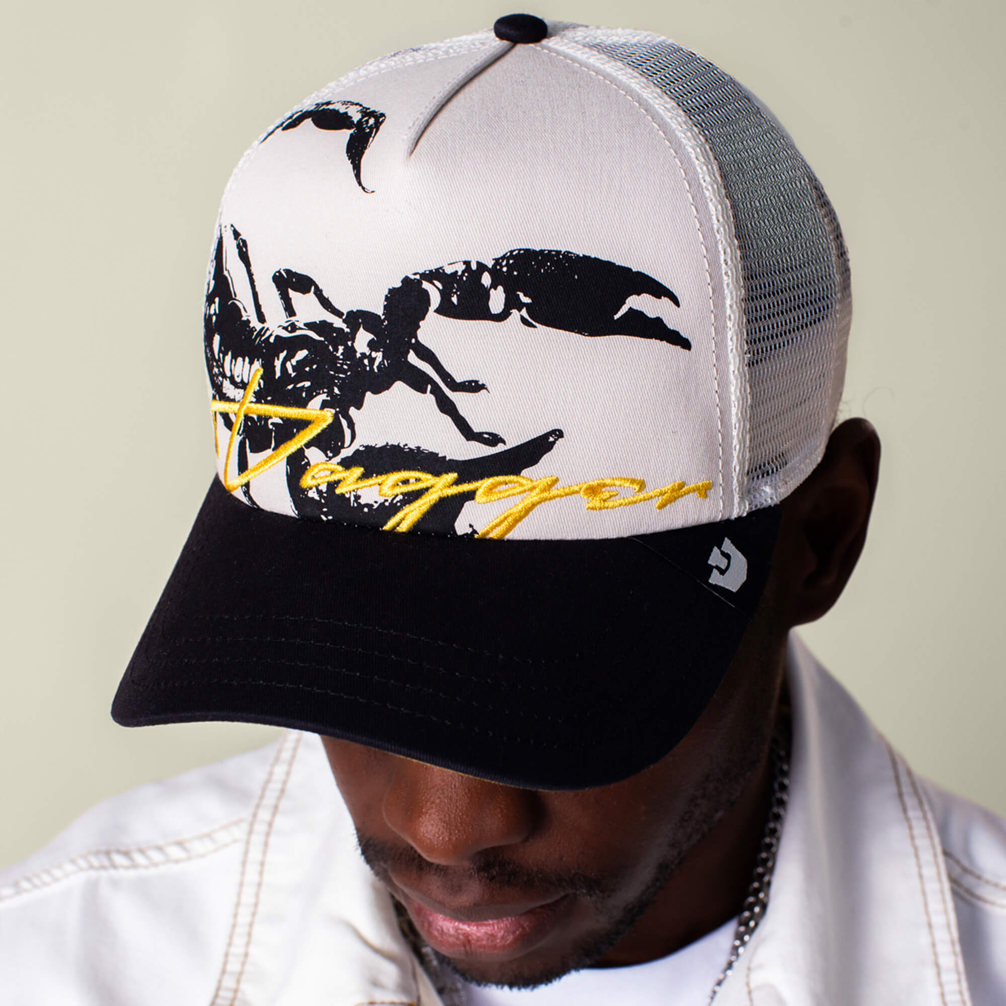 A person wearing Goorin Bros. Outside the Lines Scorpion trucker hat with a cream and black mesh back, featuring a black scorpion graphic and "Dragon" in yellow script on the front.