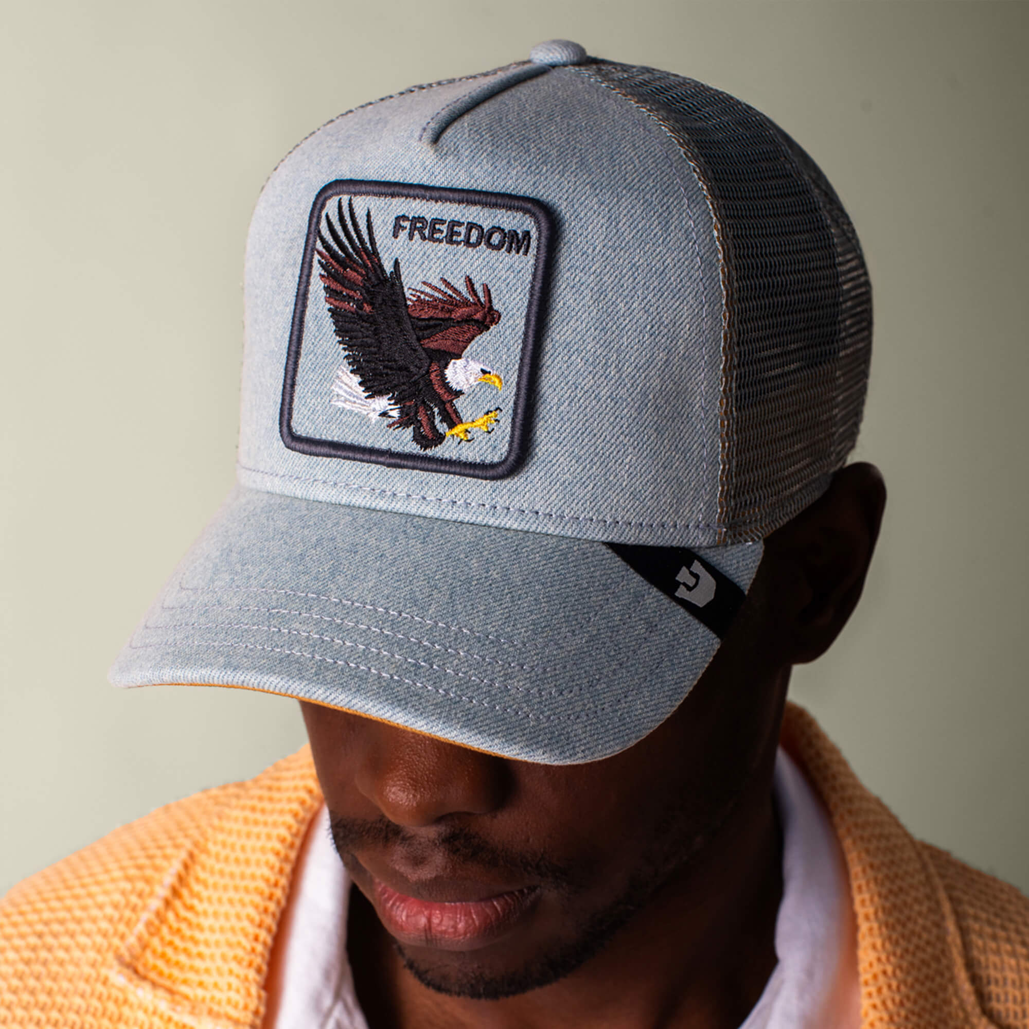 A man wears the Goorin Bros. Denim Eagle light blue baseball cap with an eagle patch and "FREEDOM" on front, styled with a yellow textured jacket over a white shirt.