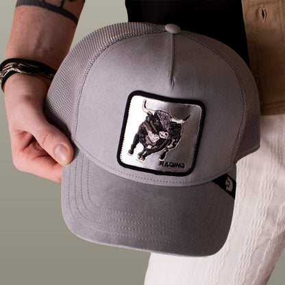 Someone holds the Goorin Bros. Silver Bull trucker cap, featuring a gray design with an embroidered black bull patch labeled "RAGING" below the image.