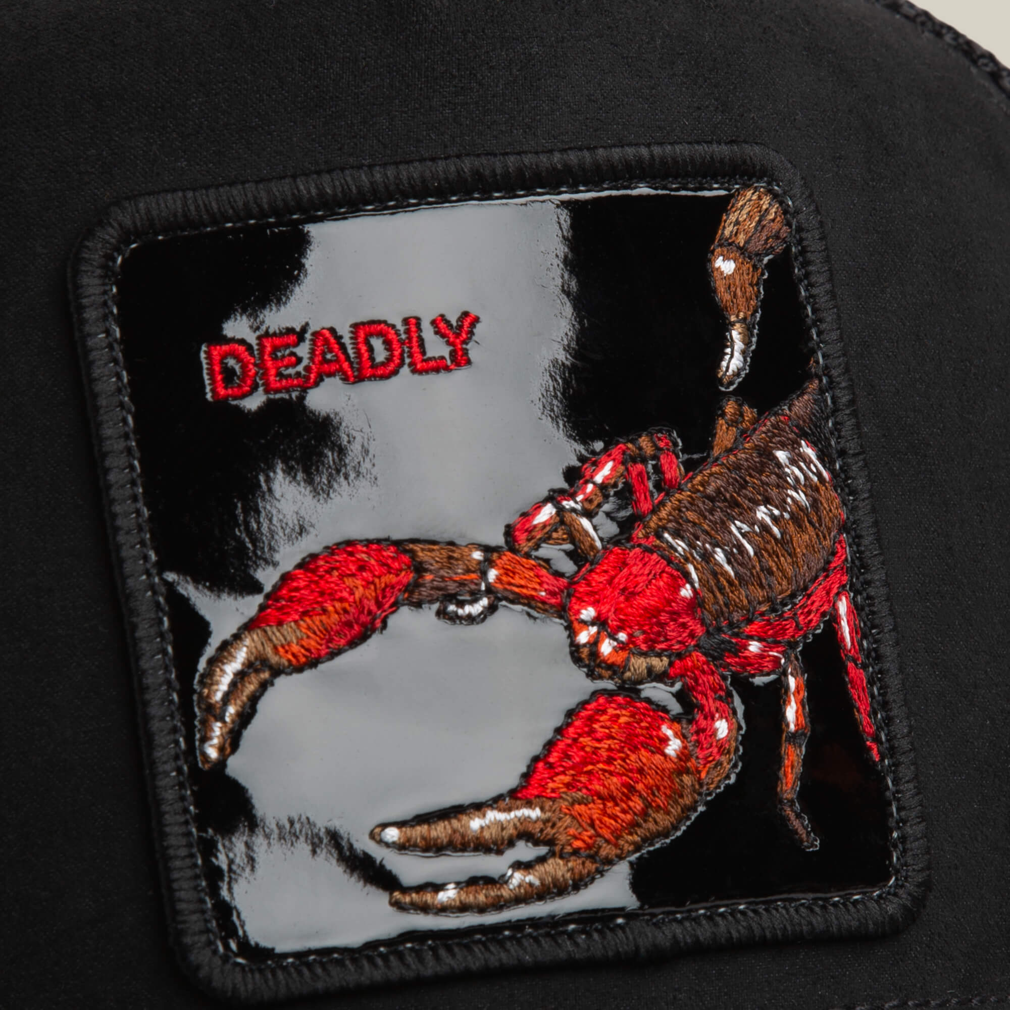 The Goorin Bros. Black Out Scorpion hat features a black suede patch with a red and brown scorpion claw and bold red "DEADLY" embroidery on a sleek black background.