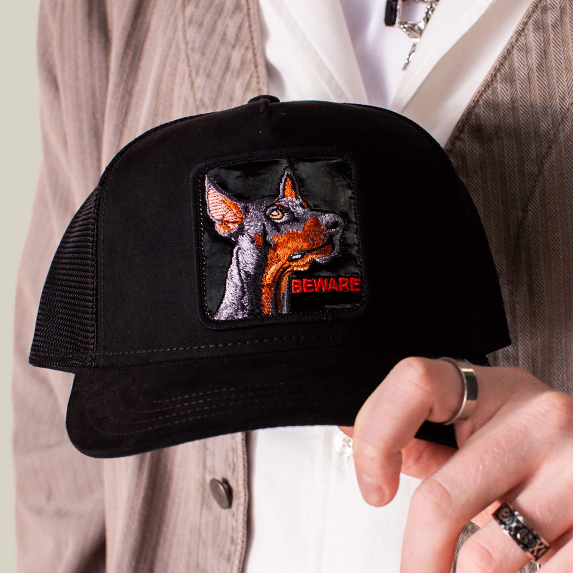 A person holding the Goorin Bros. Black Out Doberman, a black mesh baseball cap featuring an embroidered Doberman patch and "BEWARE" in red letters.