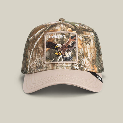 The Goorin Bros. Realtree Edge Represent Eagle cap features a camouflage color, beige brim, mesh sides, and an embroidered eagle patch with "REPRESENT" on the front.