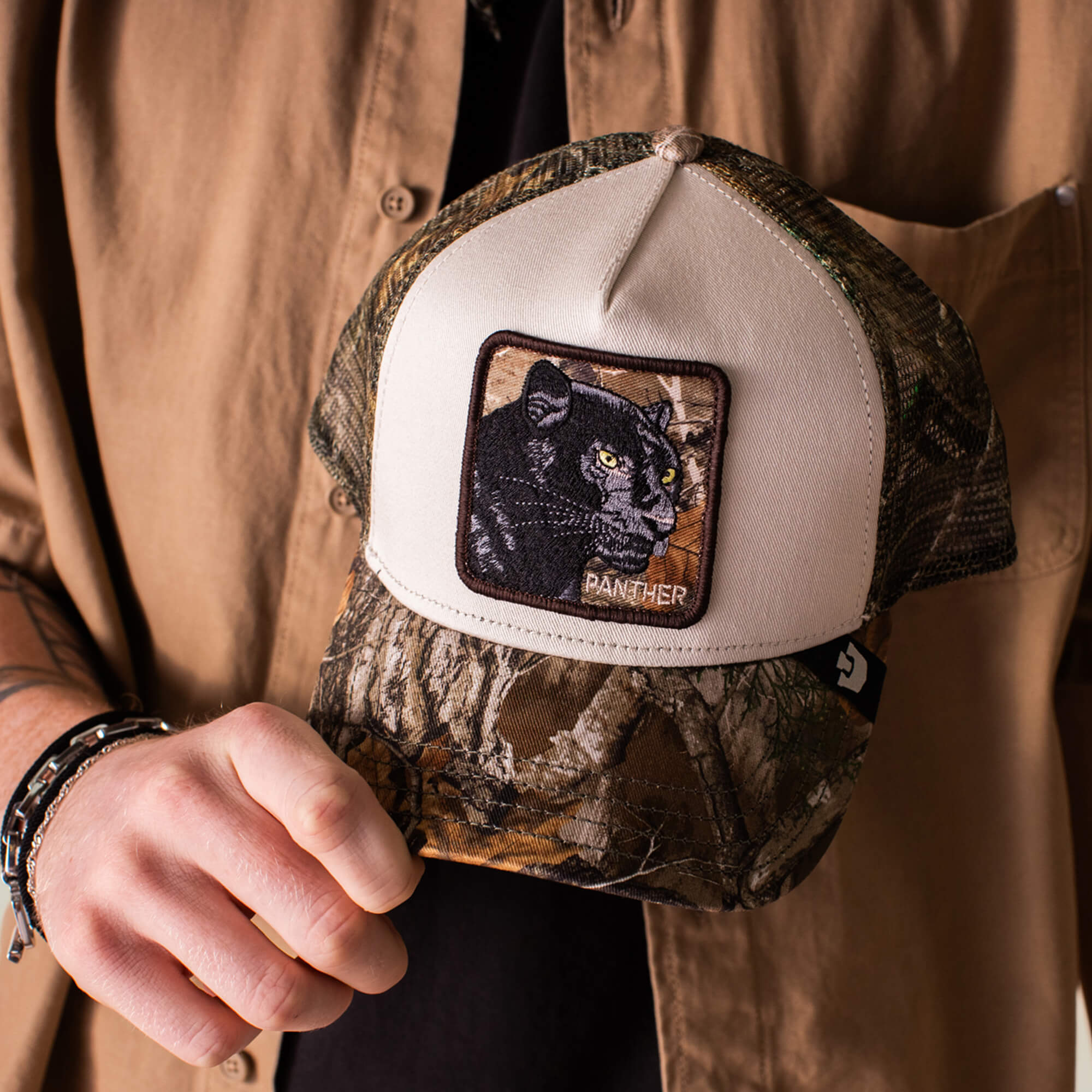 A person holds the Goorin Bros. Realtree Edge Black Panther cap, featuring camouflage print and a panther patch with "PANTHER" embroidered below.