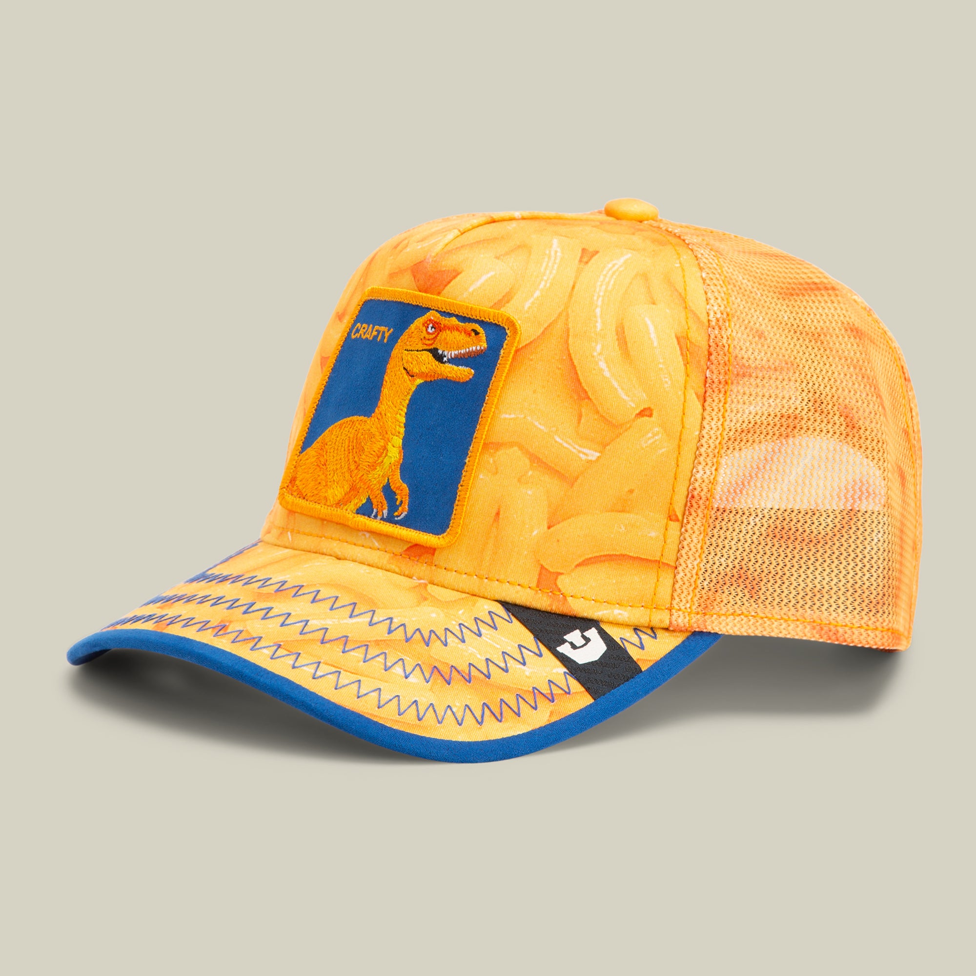 Orange and yellow mesh trucker hat with a dinosaur patch on the front panel, banana pattern, and blue accents on the brim—playful style inspired by classic American made Goorin caps.