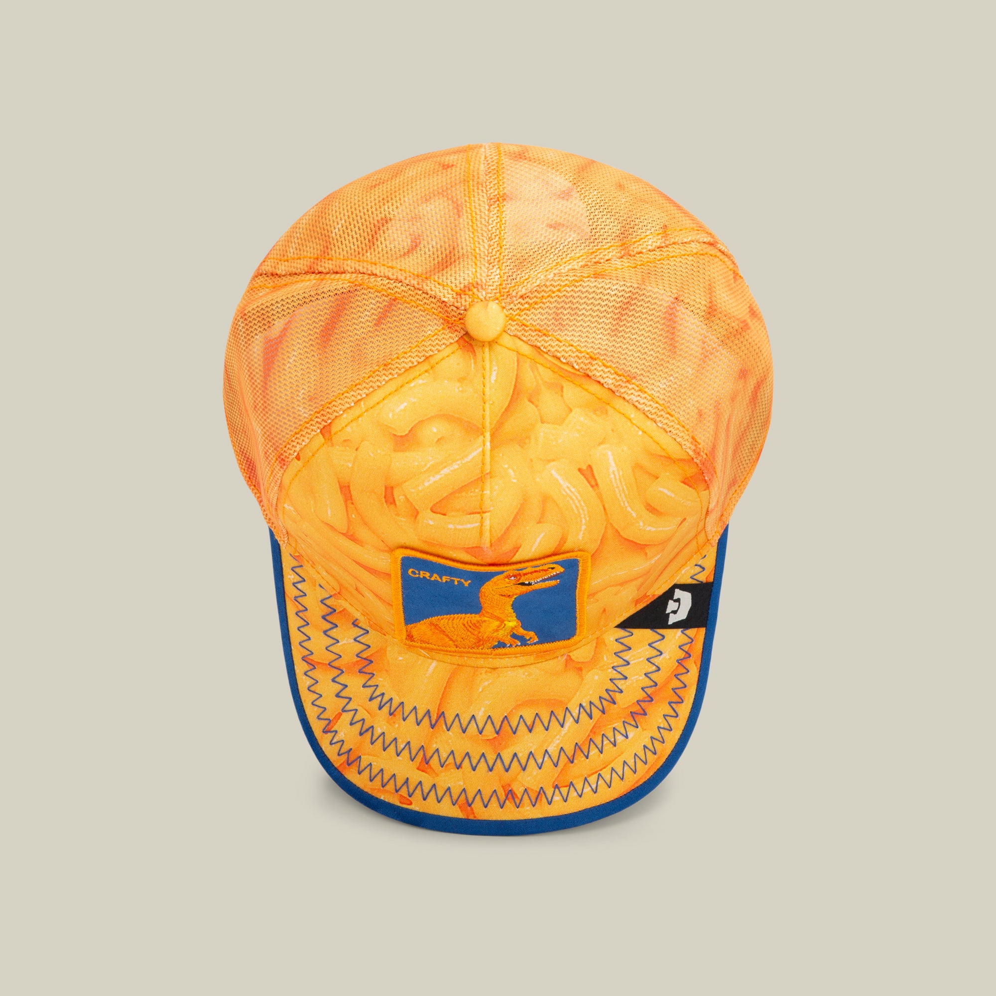 Top view of an American made orange mesh baseball cap decorated with a cheese puff pattern, a blue patch featuring a dinosaur, and blue zigzag stitching on the brim—a playful twist on bold hat designs.