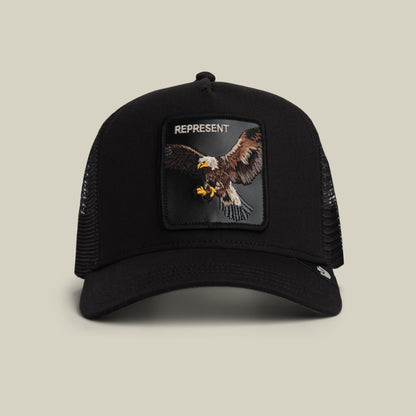 The Represent Eagle Trucker by Goorin Bros. in VOID features classic trucker style with a black mesh build and an eagle front patch, topped with "REPRESENT" embroidery. Shown against a neutral background.