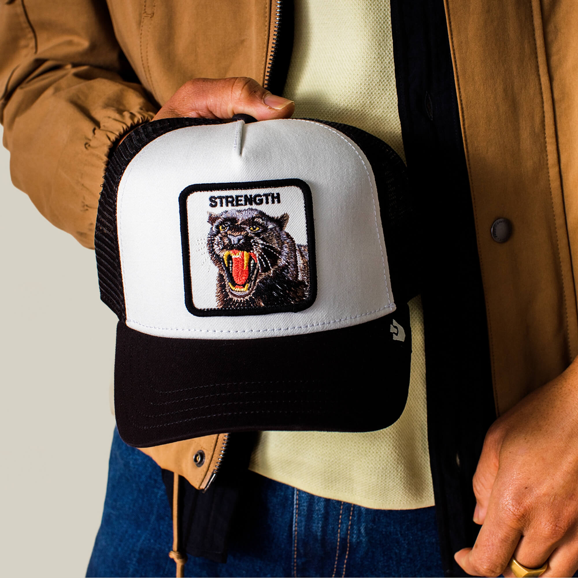 A person holds the Goorin Bros. "Strength Panther" cap, a black and white hat featuring a roaring panther patch with "STRENGTH" embroidered above it.