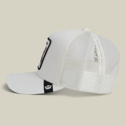 The Bestie Trucker by Goorin Bros. is a white mesh hat with a curved brim, seen from the side, featuring a black tag and a framed patch on the front panel.