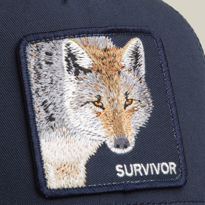 A close-up shows the Goorin Bros. Mirage Survivor navy trucker hat with an embroidered wolf patch and "SURVIVOR" stitched below it.