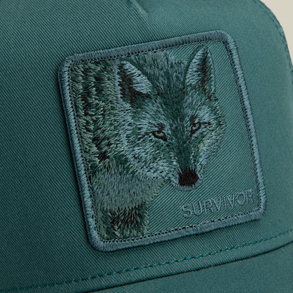 Dark teal Mirage Survivor trucker hat featuring a square patch embroidered with a wolf’s face.