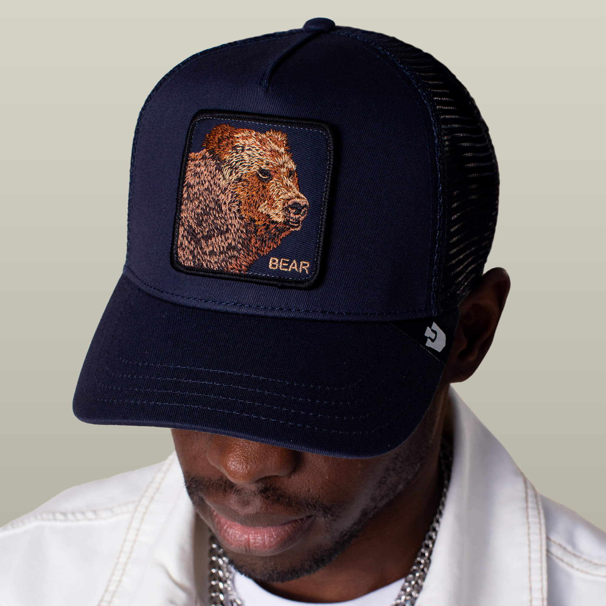 A man wearing the Goorin Bros. Bear Trucker cap, featuring a bear patch and "BEAR" embroidered on the front, looks downward.