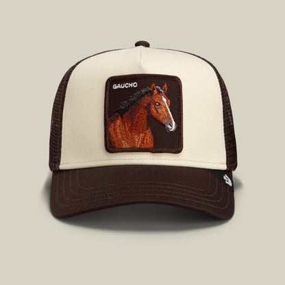 The Goorin Bros. Gaucho Trucker is a brown and beige trucker hat with an earthy colorway, featuring a rectangular patch with an embroidered horse head and the word “GAUCHO” above it.