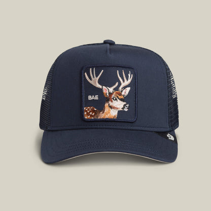 The Mirage Bae by Goorin Bros. is an EDGE-colored trucker hat with a mesh back, featuring a bold deer patch and "BAE" embroidered on the front panel.