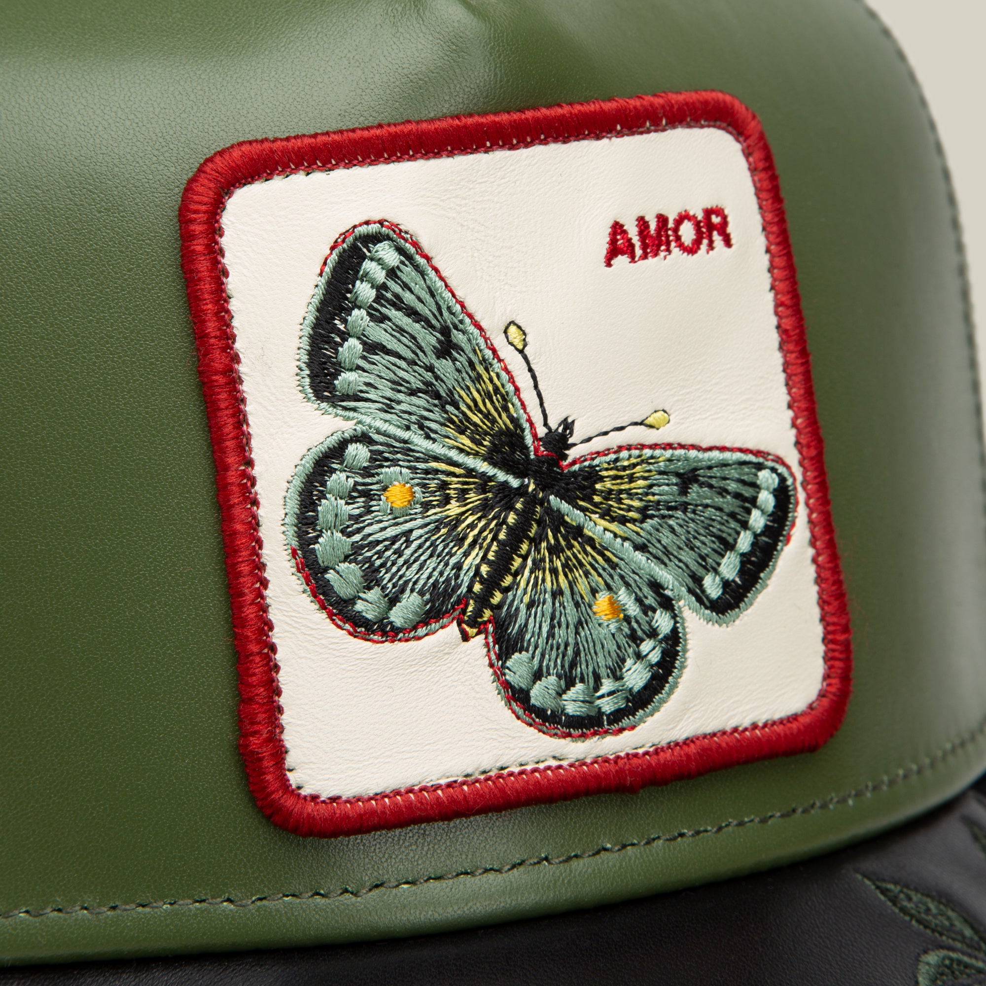 The Goorin Bros. Amor features a green leather surface, an embroidered butterfly patch with "AMOR" in red text and stitching—perfect to match with your favorite AMOR jewelry.