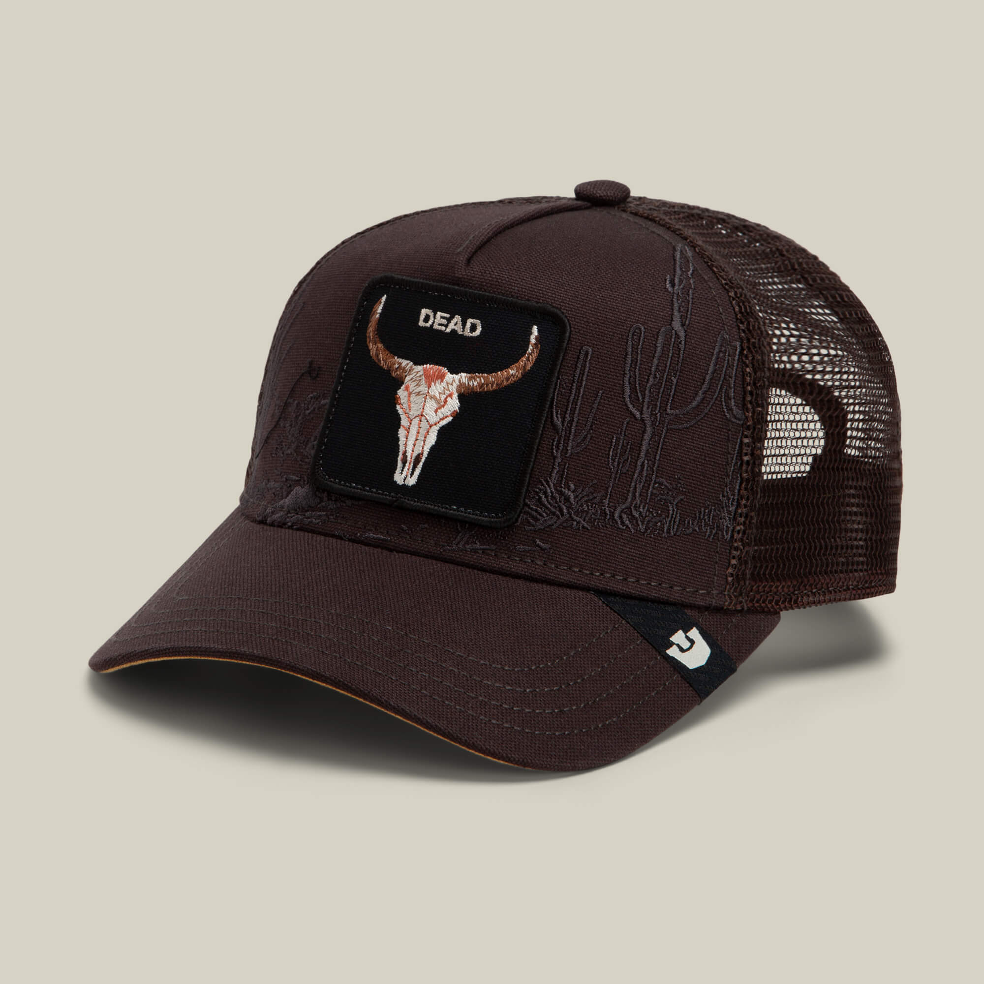 The Goorin Bros. Badlands Skull is a dark brown mesh trucker hat featuring a patch with a bull skull, the word DEAD, a cactus design, and a small logo tag on the brim.