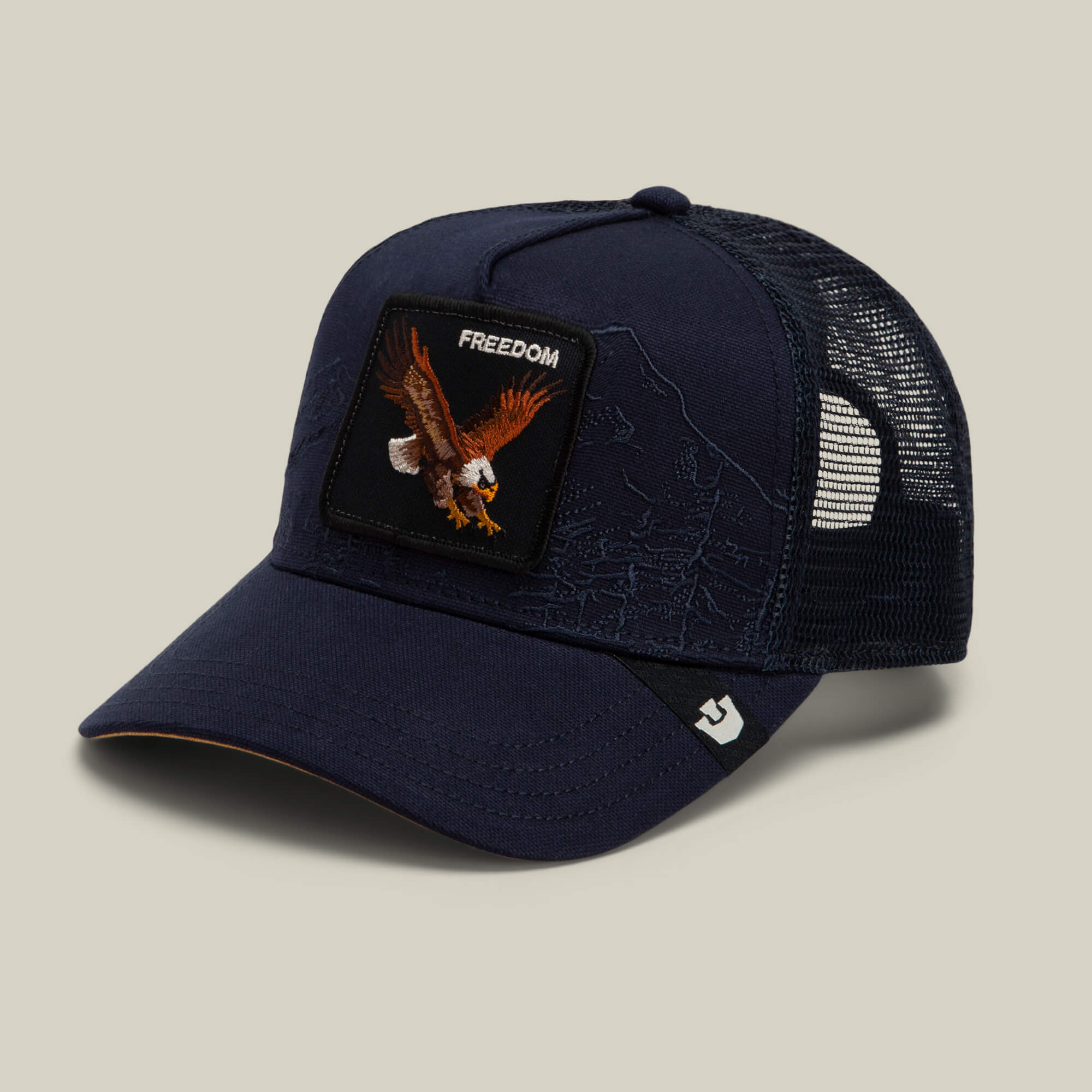 The Badlands Eagle by Goorin Bros. is a navy blue trucker hat featuring a mesh back and a front patch with an eagle and the word “FREEDOM.”.