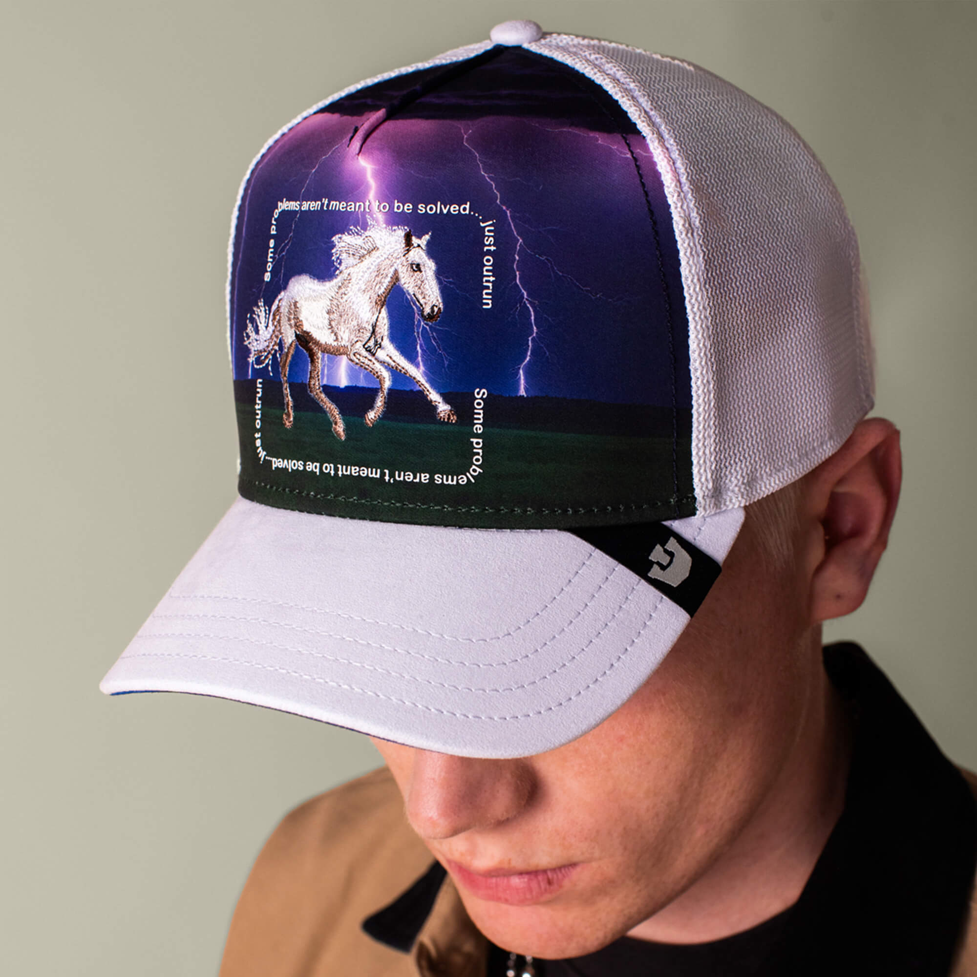 A person wears the Goorin Bros. "Through the Storm - Horse" trucker hat, featuring a running horse, lightning background, and the text: Some aren't meant to be solved, just survived.