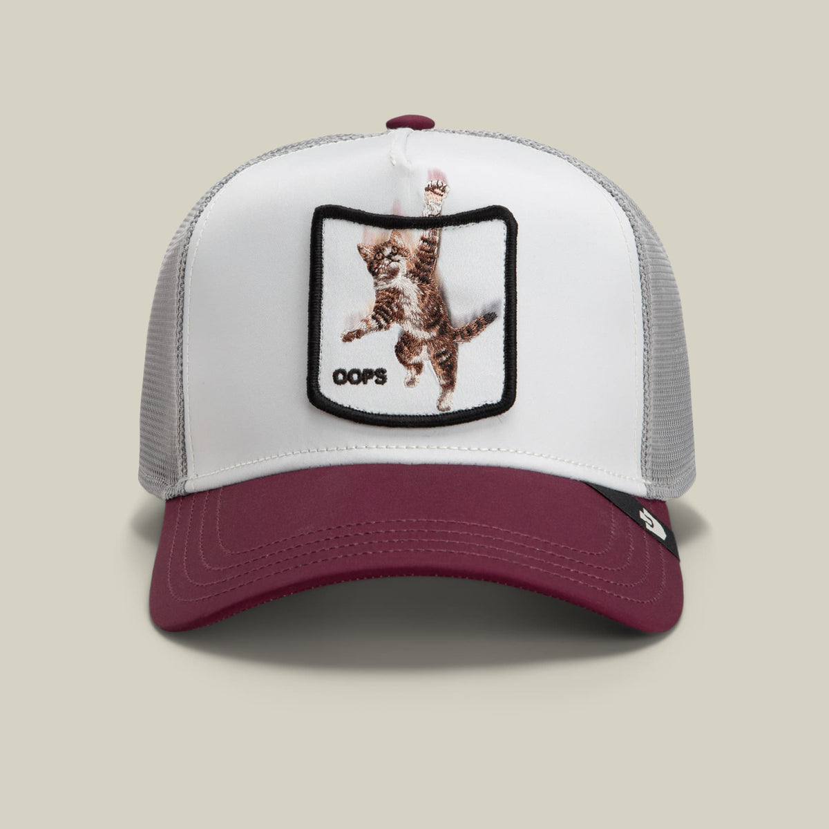 The Goorin Bros. Migration - Oops trucker hat features a white front panel and burgundy bill with gray mesh sides, highlighted by an embroidered brown cat patch with black border and "oops" text on the crown.