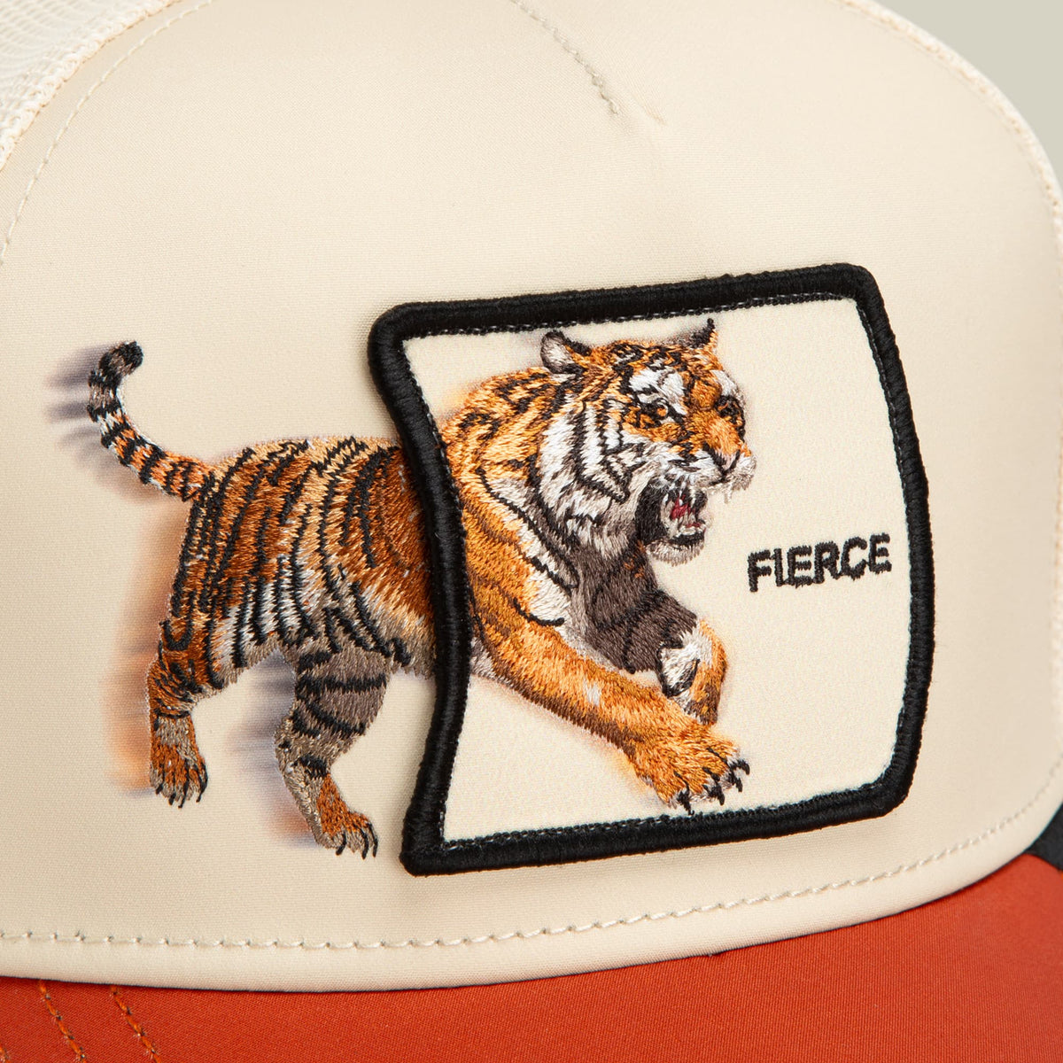 The Goorin Bros. Migration Fierce trucker hat features a cream and orange colorway with an embroidered tiger patch on the front and a striped tail extending from the side panel.