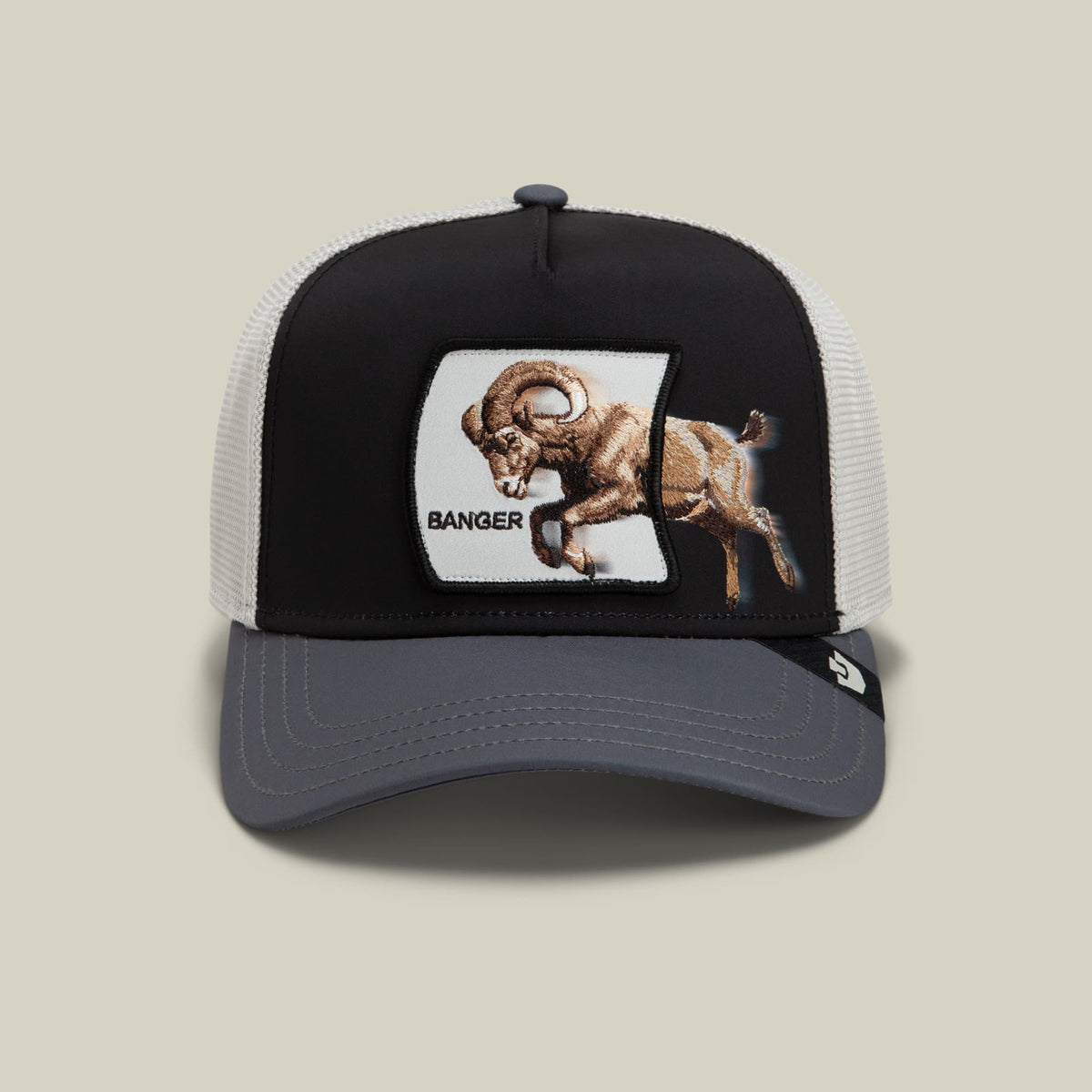 The Goorin Bros. Migration Banger trucker hat features a black front panel and white mesh back with a gray bill, showcasing an embroidered brown ram design and "Banger" text on a white patch.