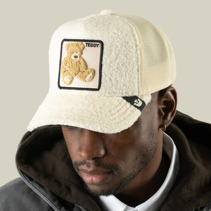 A man wears the Goorin Bros. Double Stuffed - Teddy cream sherpa trucker hat, distinguished by its plush teddy patch and “TEDDY” lettering. Paired with a dark hoodie and white collared shirt, the hat’s breathable mesh back enhances the comfort of his casual, layered style.
