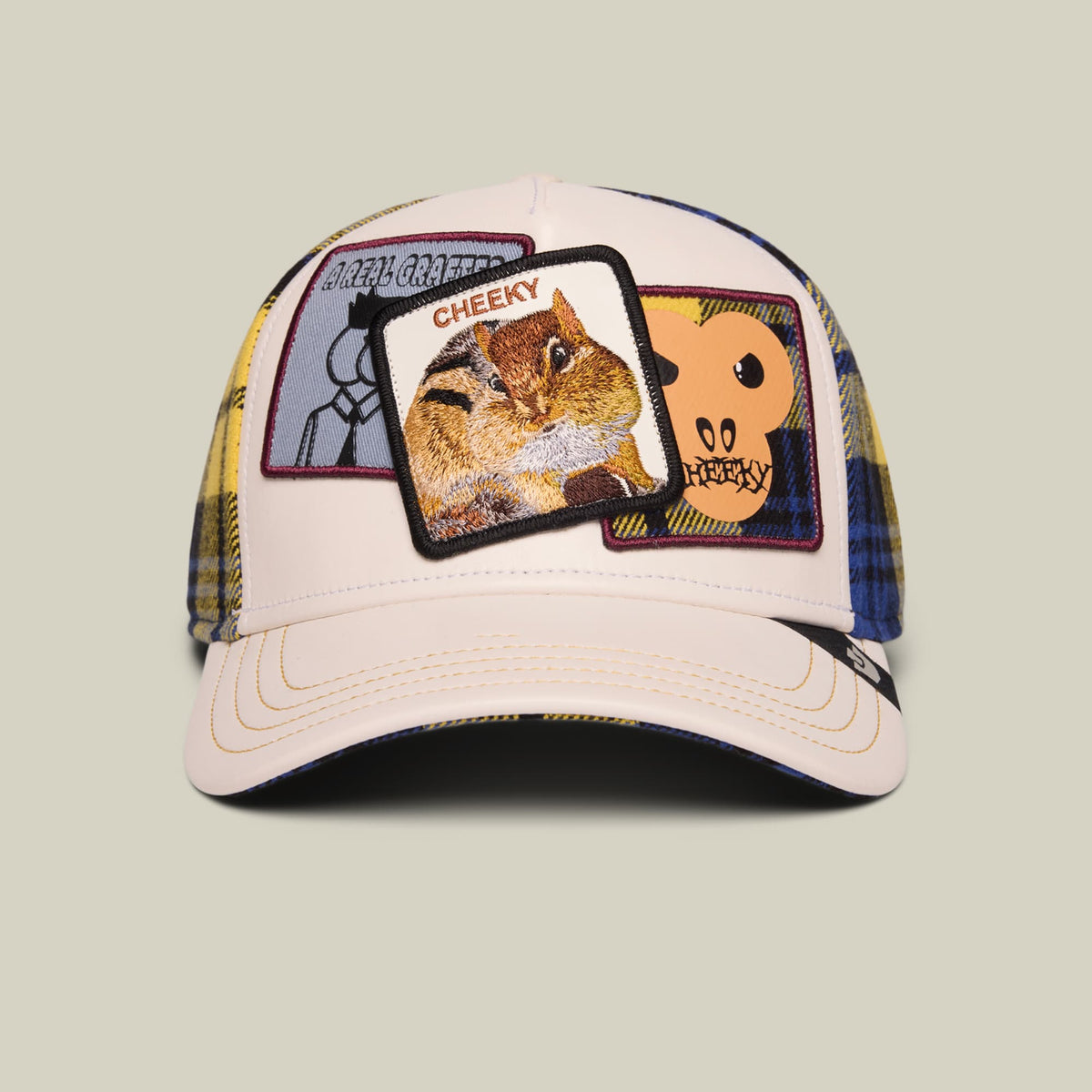 The Goorin Bros. Cheeky trucker hat features a cream front panel with embroidered animal patches including a squirrel, navy and plaid fabric on the sides, and a navy underbrim, shown on a neutral background.