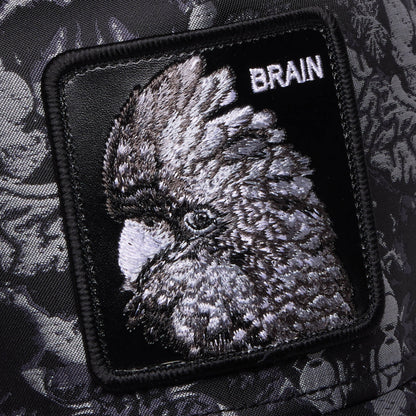 A close-up of the Goorin Bros. "Gray Matter" patch in black and grey, embroidered with a bird and the word BRAIN, set against patterned fabric—a stylish nod to intellect.