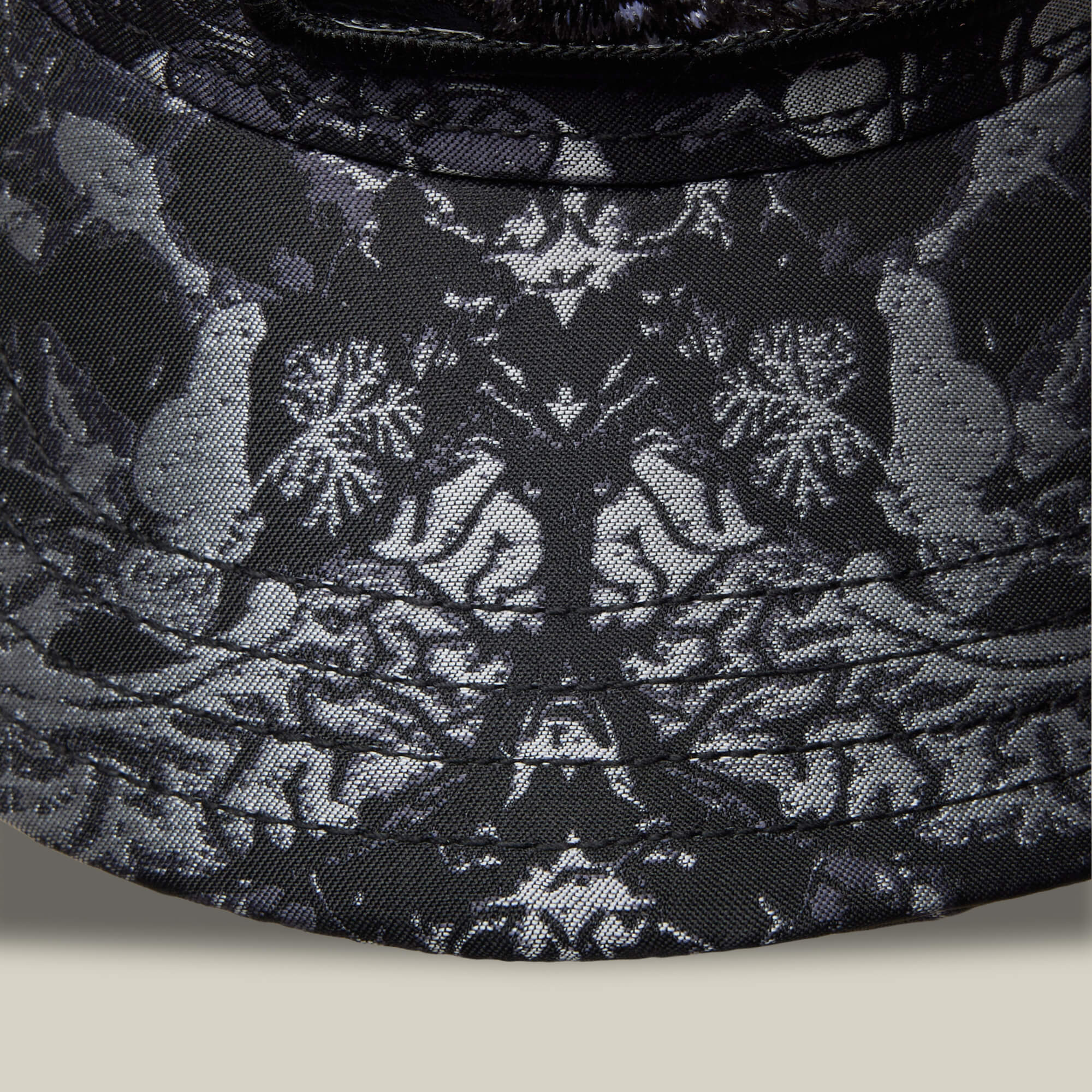 Close-up of Goorin Bros. Gray Matter: a dark fabric featuring symmetrical animal and floral patterns with light birds and flowers on a black background, inspired by intricate gray matter designs.