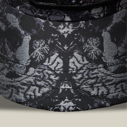 Close-up of Goorin Bros. Gray Matter: a dark fabric featuring symmetrical animal and floral patterns with light birds and flowers on a black background, inspired by intricate gray matter designs.