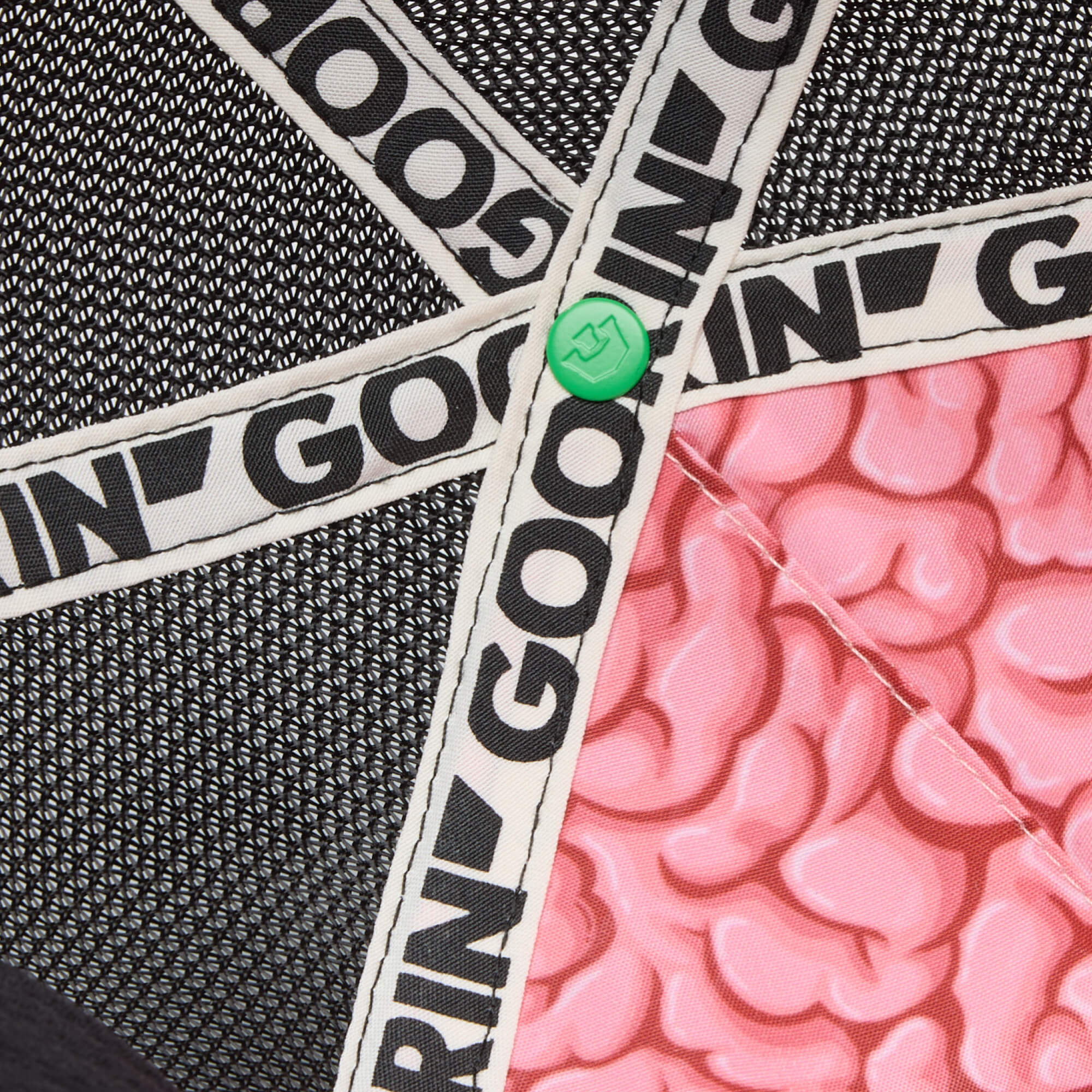 Close-up of intersecting black and white straps with "GOO" text, a green button, and pink “Gray Matter” hat texture by Goorin Bros., all set against a black mesh background.