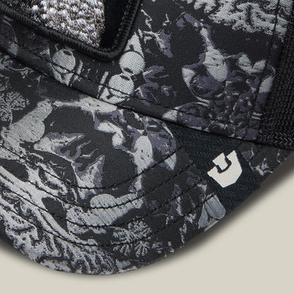 Close-up of the Goorin Bros. "Gray Matter" cap, black and gray with koi fish and aquatic plants, intricate like gray matter patterns, and a small white logo on the brim.