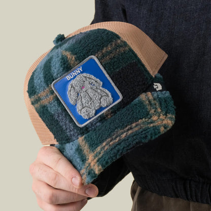 A person holds the Goorin Bros. Double Stuffed - Bunny cap: a fleece plaid baseball hat with a beige mesh back and adjustable snapback, featuring a plush gray bunny patch on a blue background labeled “BUNNY,” reminiscent of the classic Goorin trucker style.