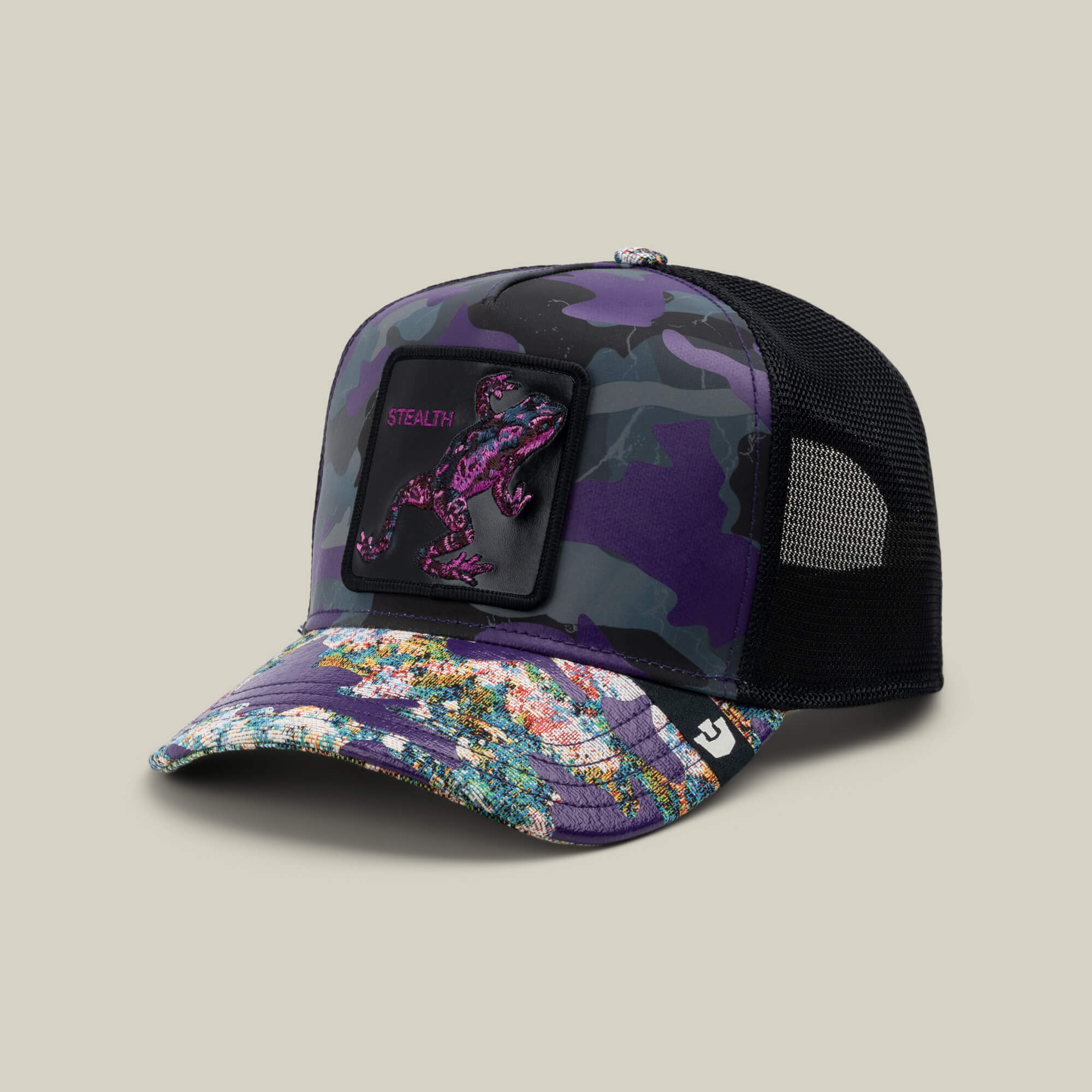 The Goorin Bros. Silent But Deadly is a purple camo trucker hat with a multicolored brim, black mesh back, and a lizard patch that says STEALTH—ideal for fans of Frogs of War style.