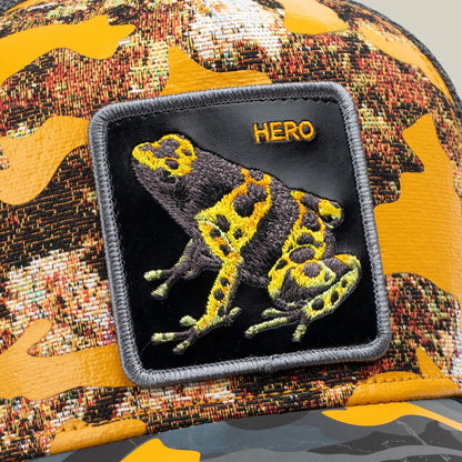 The Goorin Bros. "Knight in Sliming Armor" is a golden camo trucker hat with a yellow and black frog Hero patch featuring "HERO" boldly stitched, inspired by the Yellow Swamp Battalion.