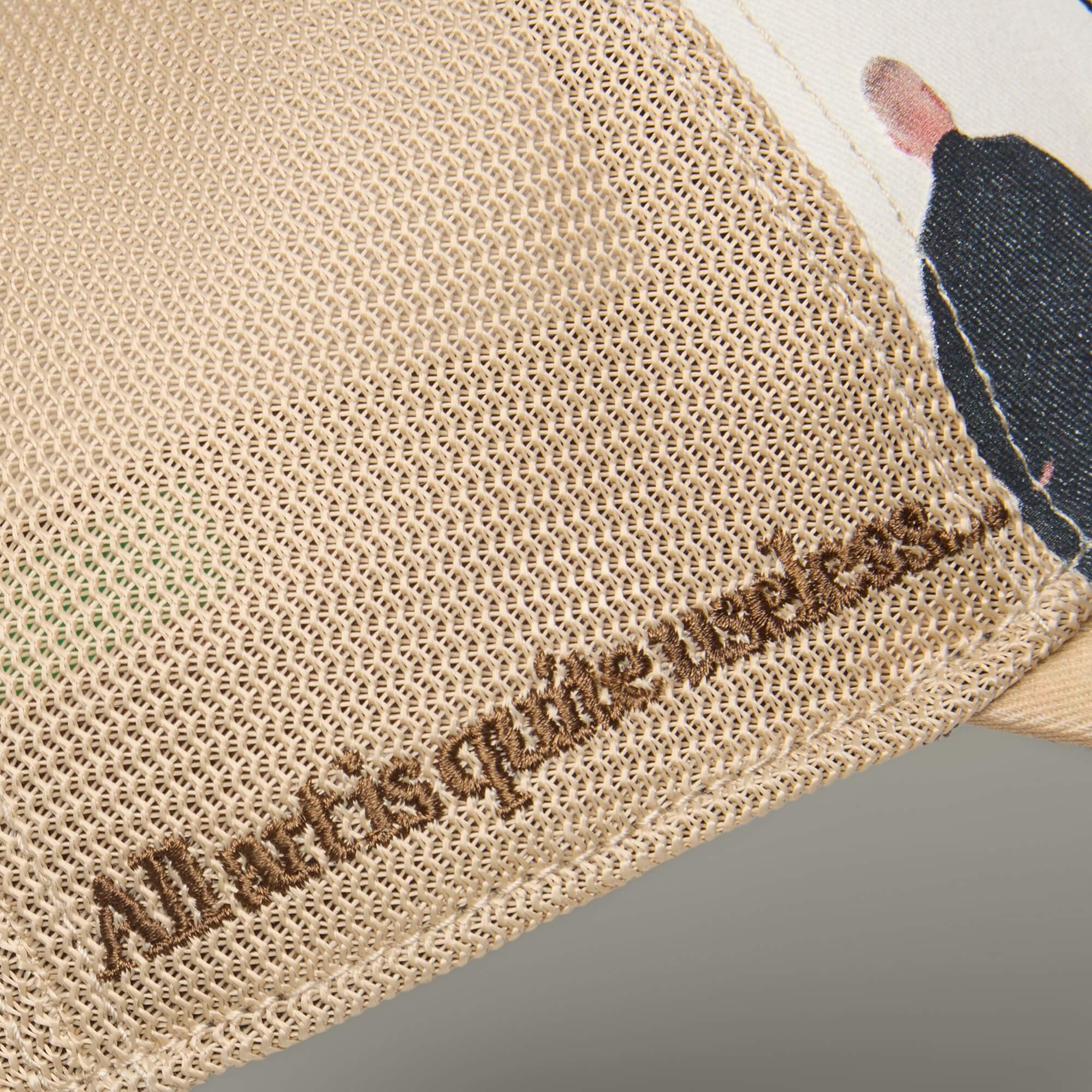 Close-up of beige mesh fabric from Goorin Bros.' Hey, I Like It! Picasso! featuring embroidered "All art is quite useless," a printed image of a person in black, and detailed digital-print embroidery for texture.