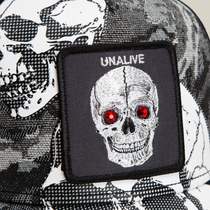 Close-up of the Goorin Bros. Bone Head Unalive trucker hat, showcasing a patch with an embroidered skull featuring red eyes and the word “UNALIVE,” a black-and-white skull pattern on the fabric, and a breathable mesh back for added comfort.